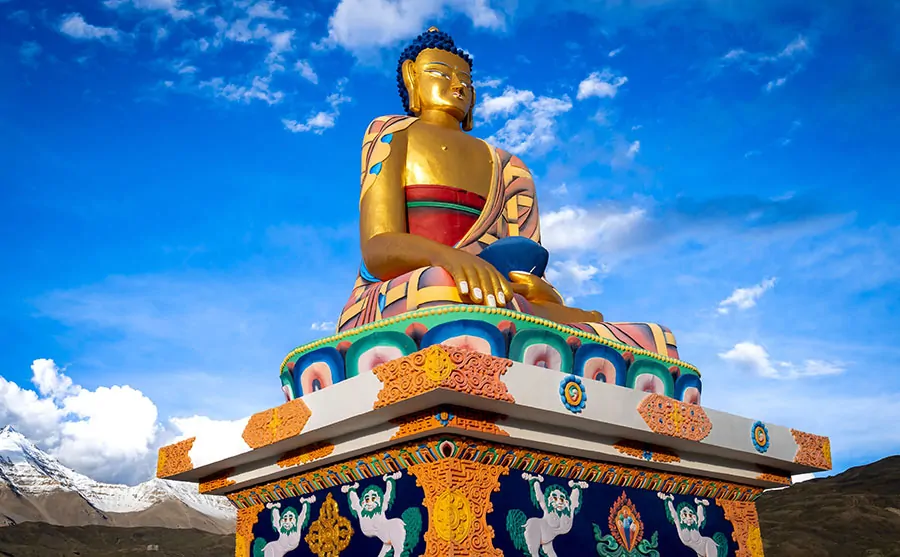Statua złotego Buddy siedzącego na ozdobnym podeście z widokiem na górski krajobraz w dolinie Spiti (Indie). Buddyzm w Indiach.