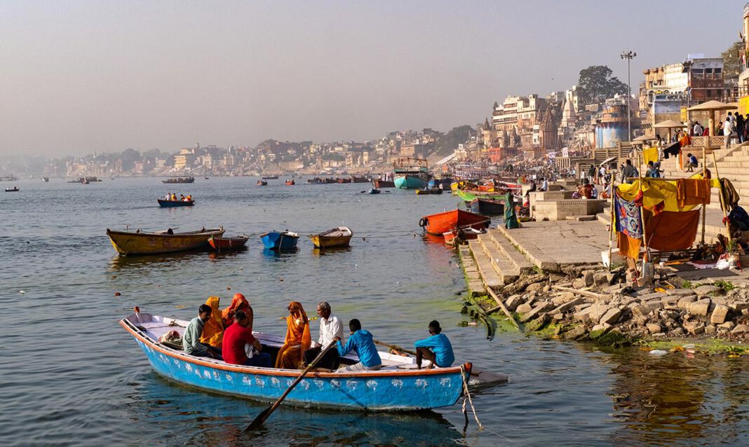 rzeki-w-indiach-swieta-rzeka-indie-ganges-jamuna-indus-brahmaputra Najświętsza rzeka Ganges, Waranasi (Indie) - kolorowe łodzie na wodzie, pielgrzymi na ghatach, zarysem miasta w tle na nieco zamglonym niebie.