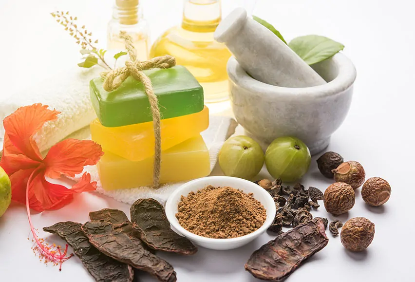 Zestaw ajurwedyjskich kosmetyków z Indii, w tym mydła w różnych kolorach, olejki, zioła i przyprawy z moździerzem.