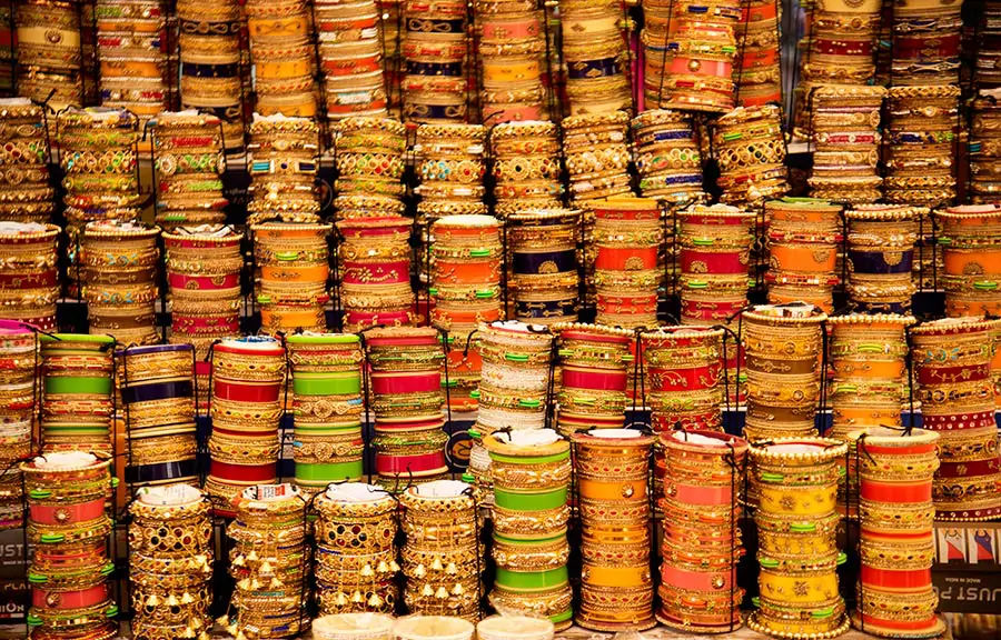 Indyjskie bransoletki i biżuteria w różnych wzorach i kolorach, ułożone w stosy.