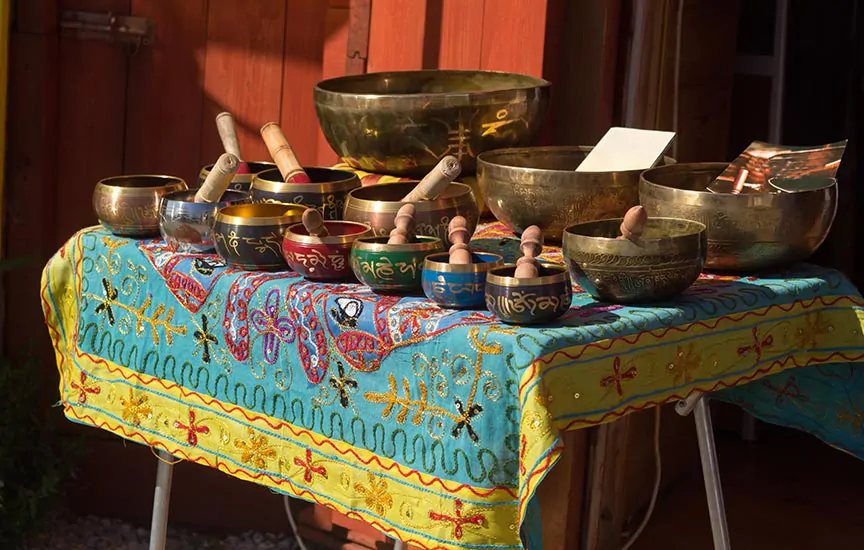 Kolorowy wybór mis tybetańskich wyłożonych na haftowanym indyjskim obrusie, każda z młoteczkiem do gry.