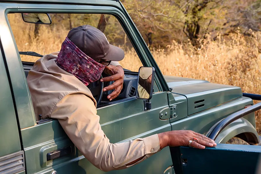 Przewodnik i kierowca na safari w Indiach siedzący w jeepie i obserwujący otoczenie, ubrany w kapelusz i maskę na twarzy.