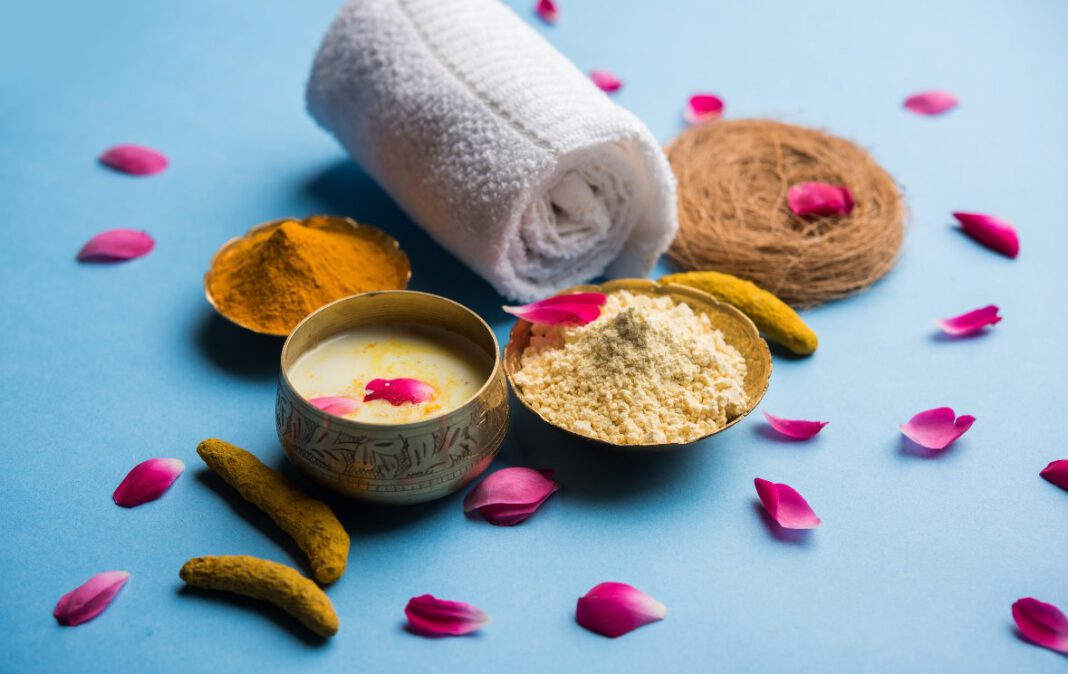 Ajurwedyjskie składniki do pielęgnacji skóry — kurkuma, mleko i płatki róż ułożone obok ręcznika na niebieskim tle.